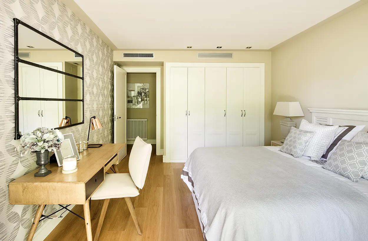 Dormitorio con espejo enmarcado en líneas horizontales, equilibrado con el escritorio y con la forma de la habitación.