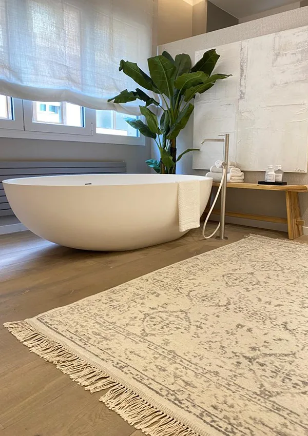 Baño en tonos neutros con cuadro para admirar desde la bañera, alfombra a conjunto y planta para dar un toque natural.