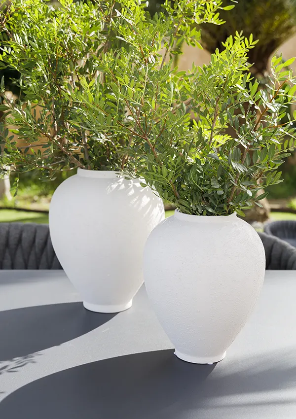 Jarrones blancos minimalistas con plantas como elementos decorativos sobre mesa exterior.