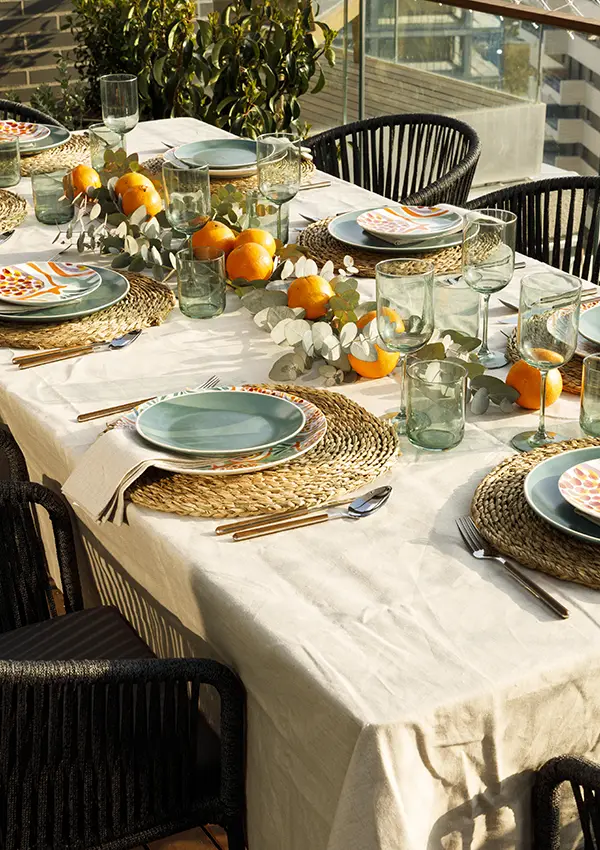 Mesa en comedor exterior con frutas decorativas y menaje en tonos turquesa y marrón.