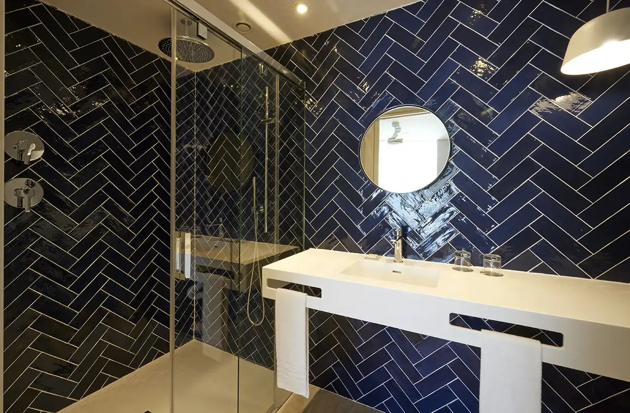 Baño contract con lavabo doble y azulejos espina de pez en color azul marino.