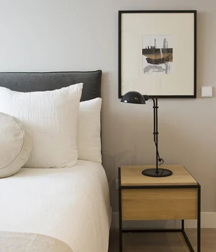Dormitorio con cama blanca y mesita de noche de madera - Apartamentos Gala Placidia