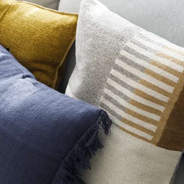 Cojines en tonos mostaza, azul marino, y neutros.