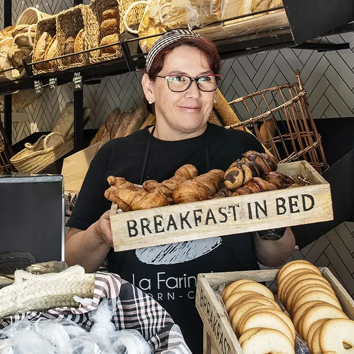 Trabajadora de la panadería mostrando una caja con croissants variados.