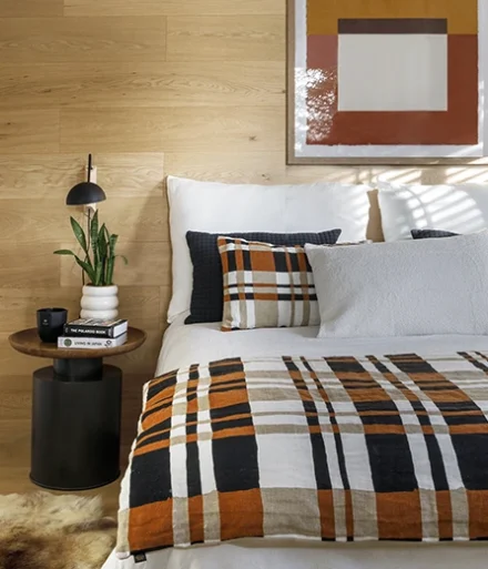 Dormitorio con pared de madera finlandesa. Sábanas, cojines y cuadros en la misma paleta de colores negro, naranja y marrón.