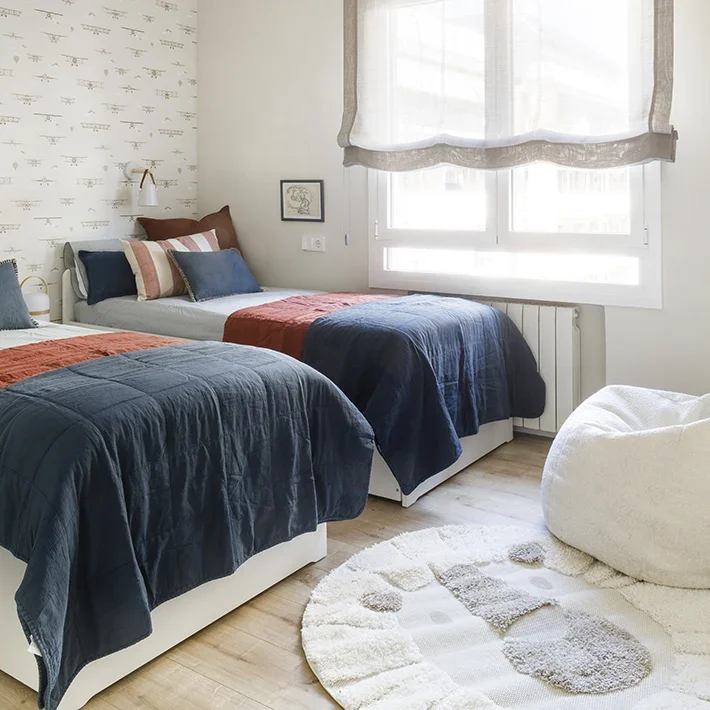 Dormitorio infantil con pared estampada de aviones y camas individuales con colores azul marino y terracota.