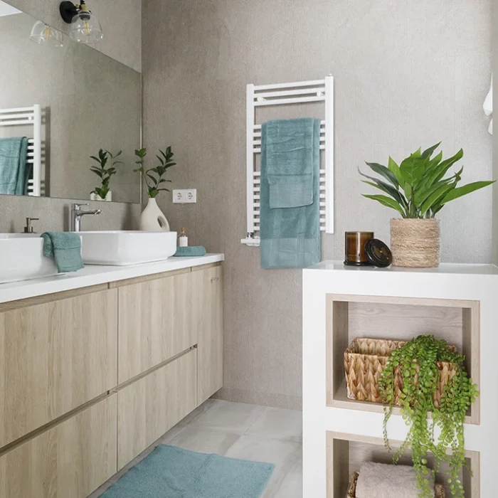 Lavabo con pared y suelo grises, mobiliario blanco y de madera clara. Decorado con plantas en macetas naturales o abstractas y toallas de color azul.