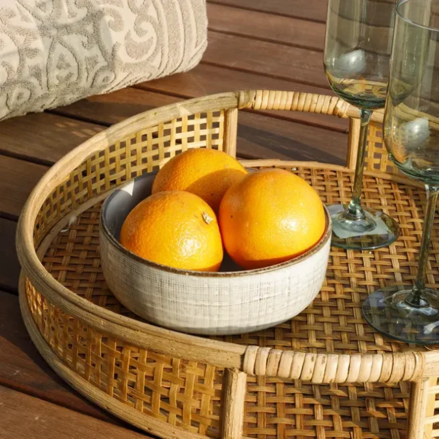 Bandeja de mimbre con frutas y copas en mesa exterior.