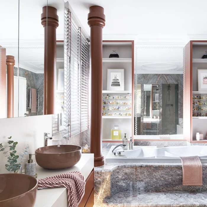 Baño con estética barroca suave en tonos rojizos y mármol oscuro.