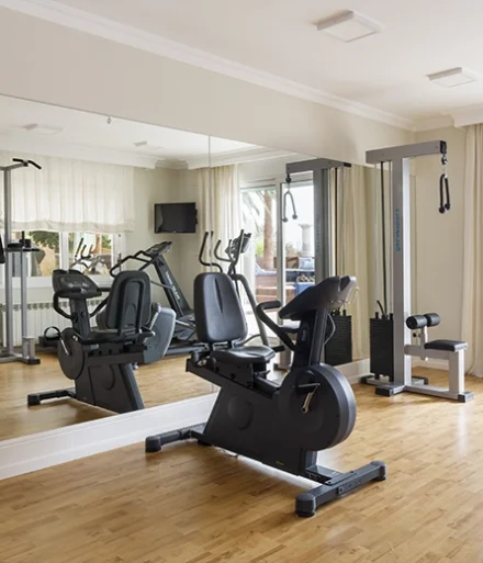 Gimnasio con máquinas de fuerza y cardio frente a pared espejo.