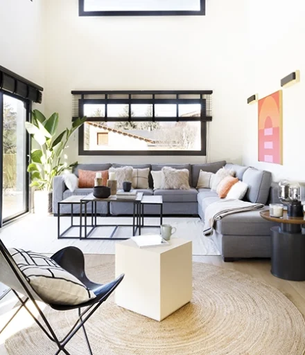 Salón con sofá esquinero de color gris, conjuntado con dos mesas auxiliares en la misma gama cromática.