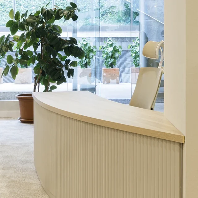Rincón de trabajo con mesa de madera clara y silla de oficina en color beis.