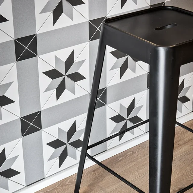 Patrón ecléctico en pared, junto suelo de madera y taburete negro