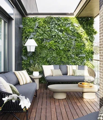 Terraza exterior con sofás oscuros y cojines verdes y crema, a juego con las mesas y plantas.